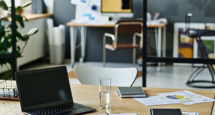 Workplace of economist or accountant with laptop, notebook with pen, glass of water and financial documents in openspace office